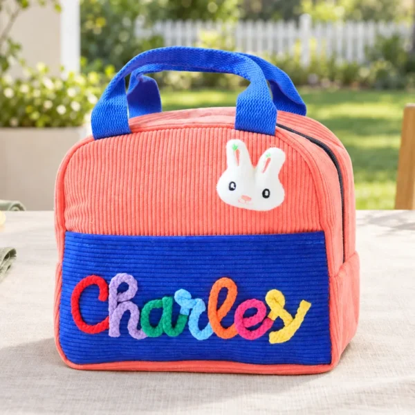 Personalized insulated corduroy lunch bag in coral and royal blue with raised yarn name lettering.