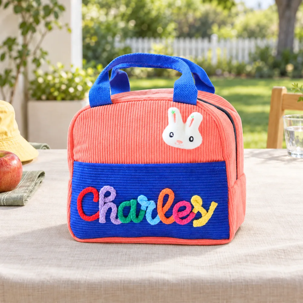 Personalized insulated corduroy lunch bag in coral and royal blue with raised yarn name lettering.